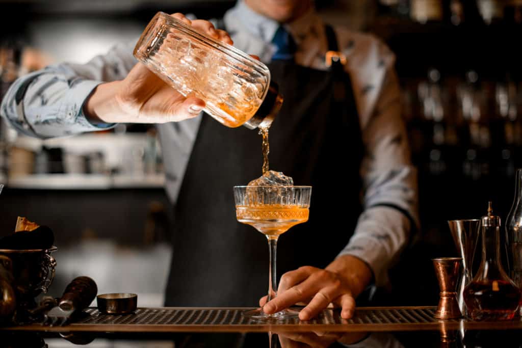 Barman pouring drink from cocktail shaker into cocktail glass