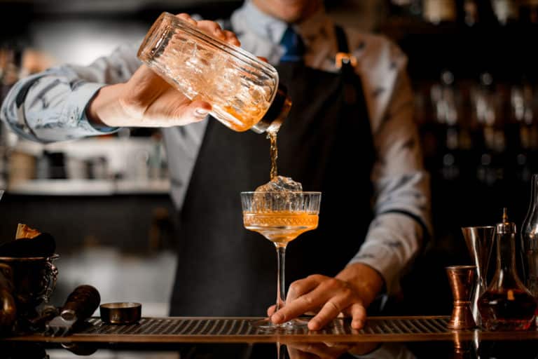 Barkeeper gießt ein Getränk aus dem Cocktailshaker in ein Cocktailglas