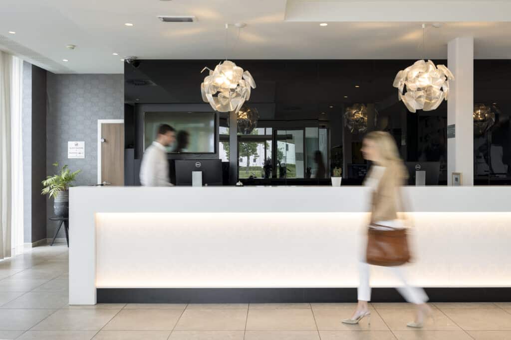 Hotel reception with employee walking behind desk and woman walking in front of the desk.