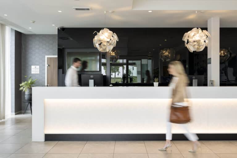 Hotelreceptie met een medewerker die achter de balie loopt en een vrouw die voor de balie loopt.